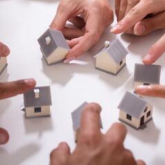 Hands moving mini homes around a white surface