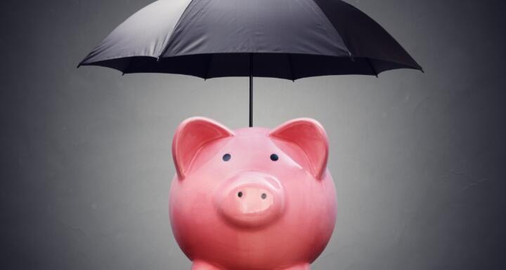 A pink ceramic piggy bank under a black umbrella signifying financial safety net