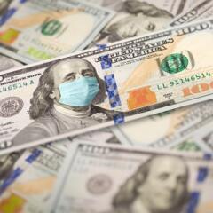 Pile of one hundred dollar bills with medical face mask on the Benjamin Franklin on the top bill