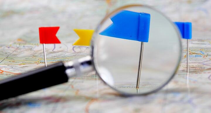 Flag pins pushed into a map, with a magnifying glass highlighting a blue pin