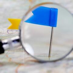 Flag pins pushed into a map, with a magnifying glass highlighting a blue pin