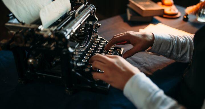 Portrait of bearded literature author in glasses typing on vintage typewriter