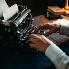 Portrait of bearded literature author in glasses typing on vintage typewriter