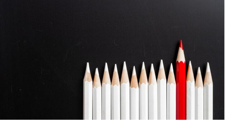 Line of white pencils all the same height with one red pencil in the middle and sticking up higher