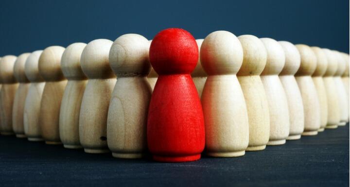 Red wooden figure in front on plain wooden figures