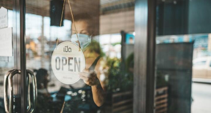 Restaurant worker with mask flipping open sign in window