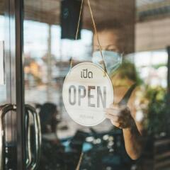 Restaurant worker with mask flipping open sign in window
