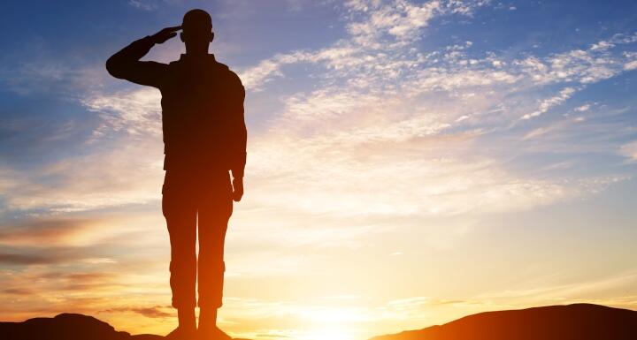 silhouette of a soldier standing and saluting with a sunset in the background