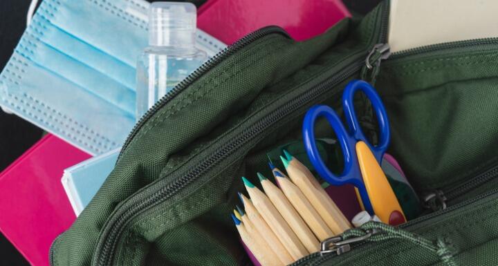 A student's backpack with pencils, scissors, hand sanitizer, and a medical mask