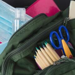 A student's backpack with pencils, scissors, hand sanitizer, and a medical mask