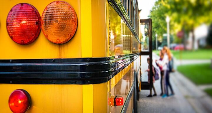 Rear corner of school bus with children loading on in background