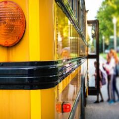 Rear corner of school bus with children loading on in background