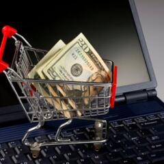Tiny metal shopping cart sitting on the keyboard of a laptop with folded twenty dollars in it