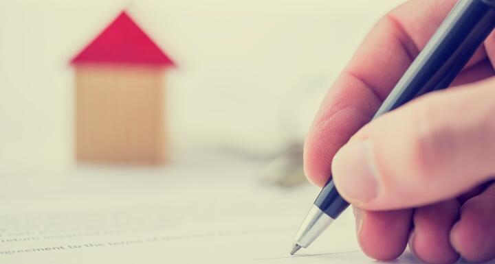 Hand signing the deed to a house with a house in the background