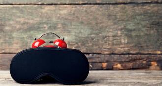 A black sleeping mask on top of a red alarm clock