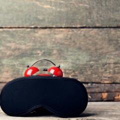 A black sleeping mask on top of a red alarm clock