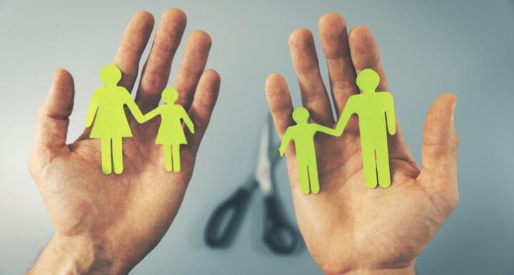 small paper cutouts of a family with different members in each hand and scissors in the background