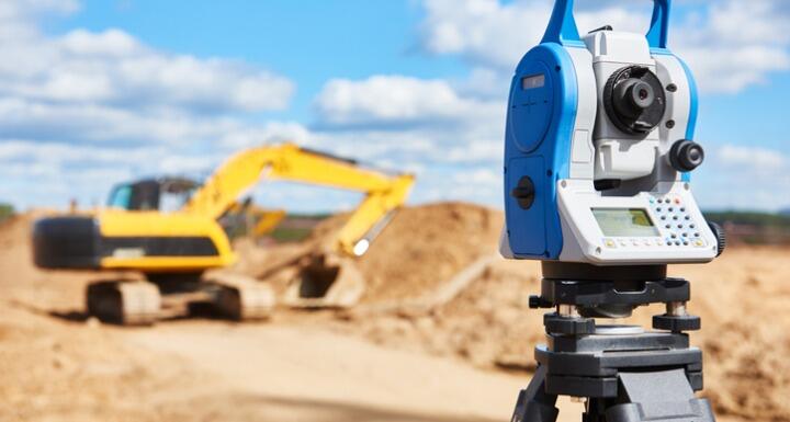 Surveyor equipment in the foreground with a yellow construction truck in the background