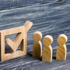 Three wooden human figures stand together next to a tick in the box