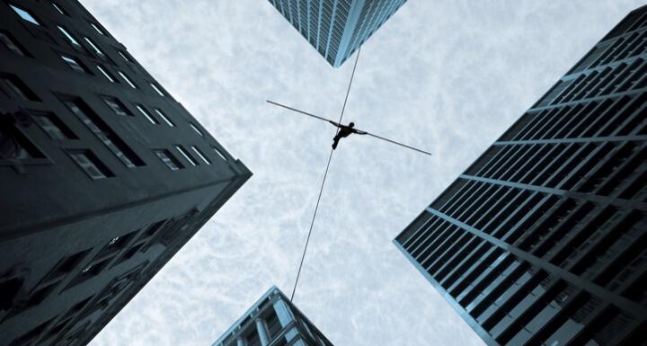 Bottom up view of a person on tightrope walking between buildings