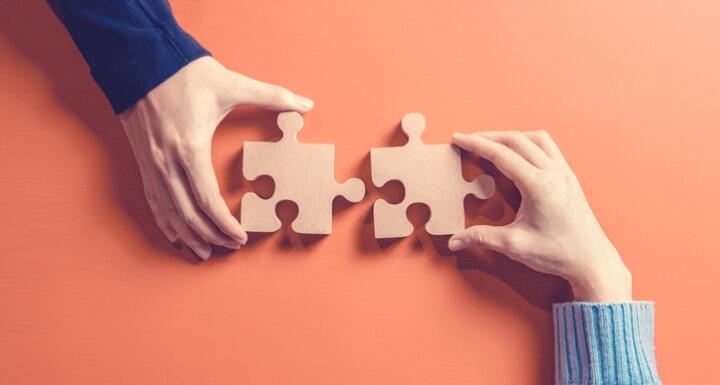 Two hands holding jigsaw on orange background