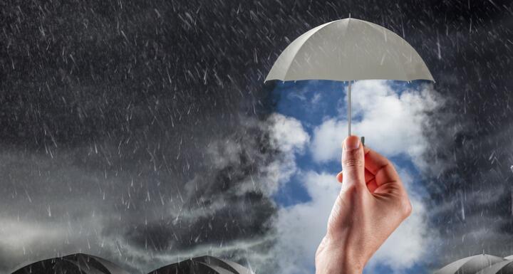 Hand holding umbrella breaking through stormy skies to reveal blue sky with clouds