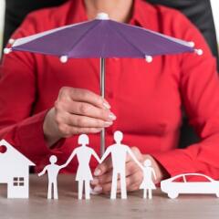 Woman holding a toy umbrella over a set of paper dolls and their paper house and car