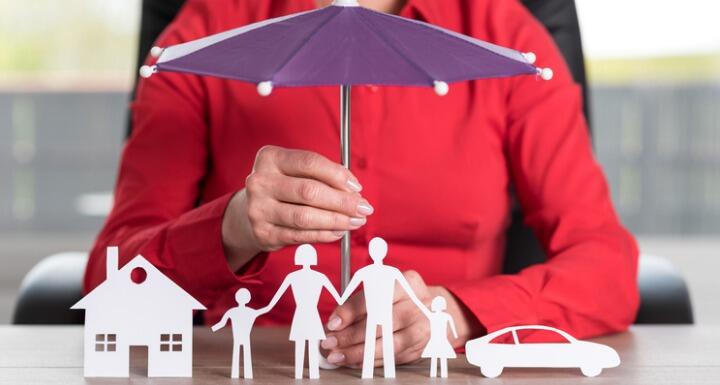 Woman holding a toy umbrella over a set of paper dolls and their paper house and car