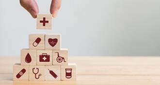 Wood blocks with health care icons stacked in pyramid with a hand placing the top block