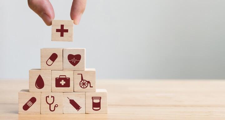 Wood blocks with health care icons stacked in pyramid with a hand placing the top block 