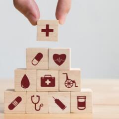 Wood blocks with health care icons stacked in pyramid with a hand placing the top block 