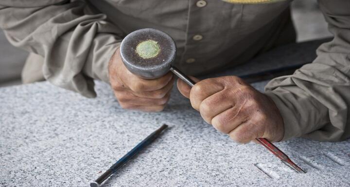 A stonemason working on granite with a chisel