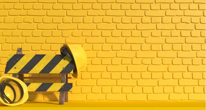 Yellow hard hats on yellow caution barrier in front of yellow brick wall