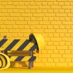 Yellow hard hats on yellow caution barrier in front of yellow brick wall