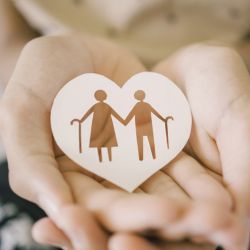 Young hand holding cutout of paper heart with elderly couple