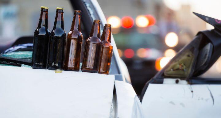 Beer bottles on hood of white car at accident scene with flashing lights of cop car in background