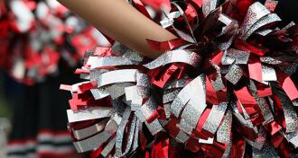 Cheerleader hand holding a red silver and black pom pom behind their back