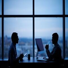 Two shadowy figures talking in front of large office windows