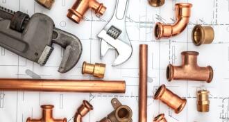 Plumbing wrenches and pieces of copper piping on an architectural drawing background