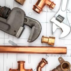 Plumbing wrenches and pieces of copper piping on an architectural drawing background
