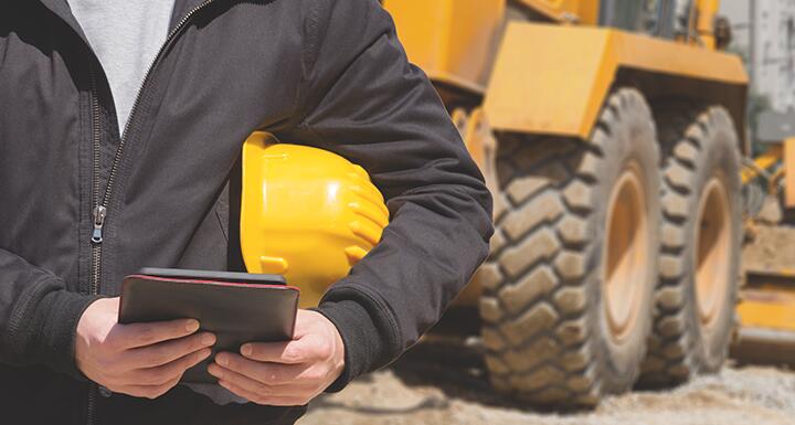 Close up of man with hard hat under arm and tablet in hands on a construction site