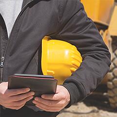 Close up of man with hard hat under arm and tablet in hands on a construction site