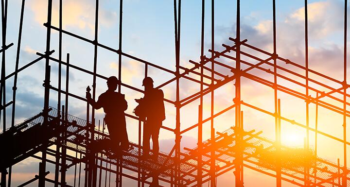 Construction workers on scaffolding with a sunset in the background