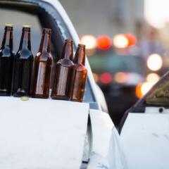 Beer bottles on hood of white car at accident scene with flashing lights of cop car in background