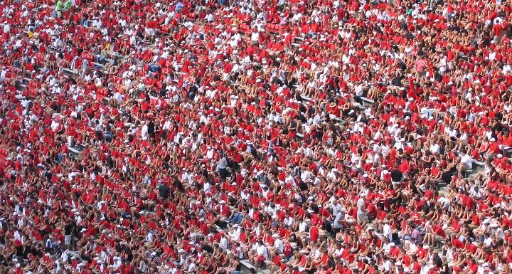 By fans standing to watch a college football game