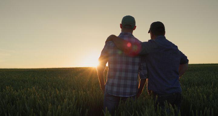 Father farmer hugging his adult son and watching the sunset