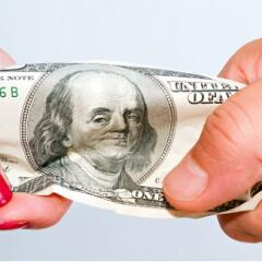 two hands each holding one end of a hundred dollar bill