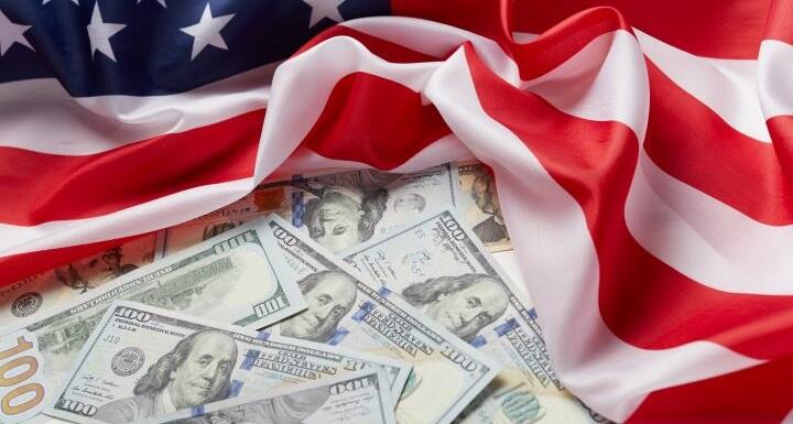 Several one hundred dollar bills arranged on top of an American flag