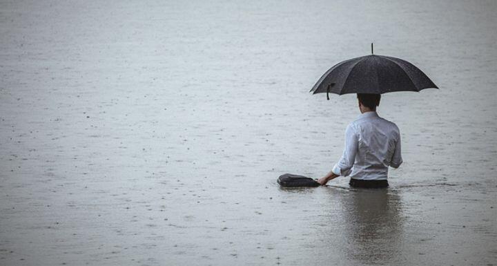 man standing in water and holding umbrella during rain