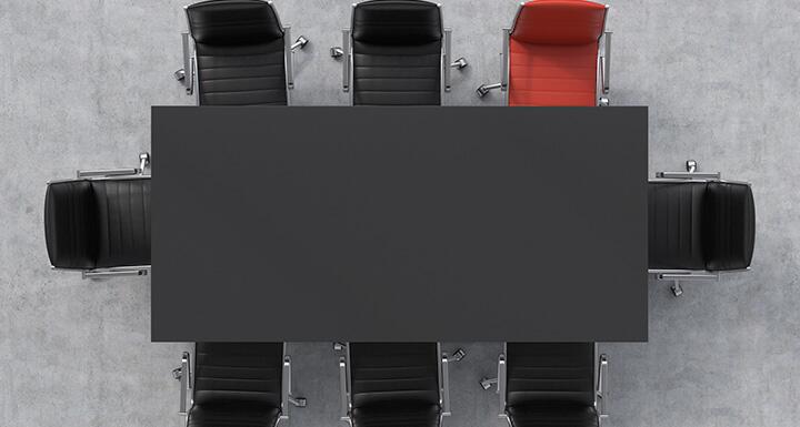 Looking down from above on a black conference room table with 7 black chairs and 1 red chair